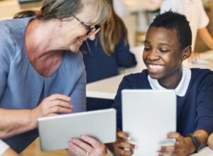 Professora com aluno, ambos com um tablet na mão e sorrindo